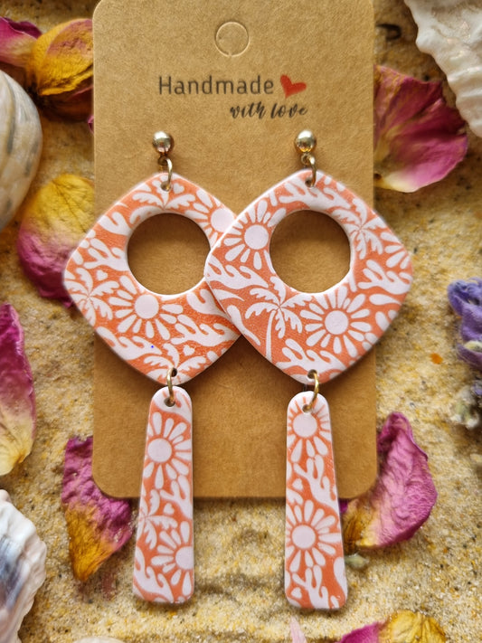 Handmade polymer-clay dangle earrings featuring cream daisies & tropical palms on a tangerine background