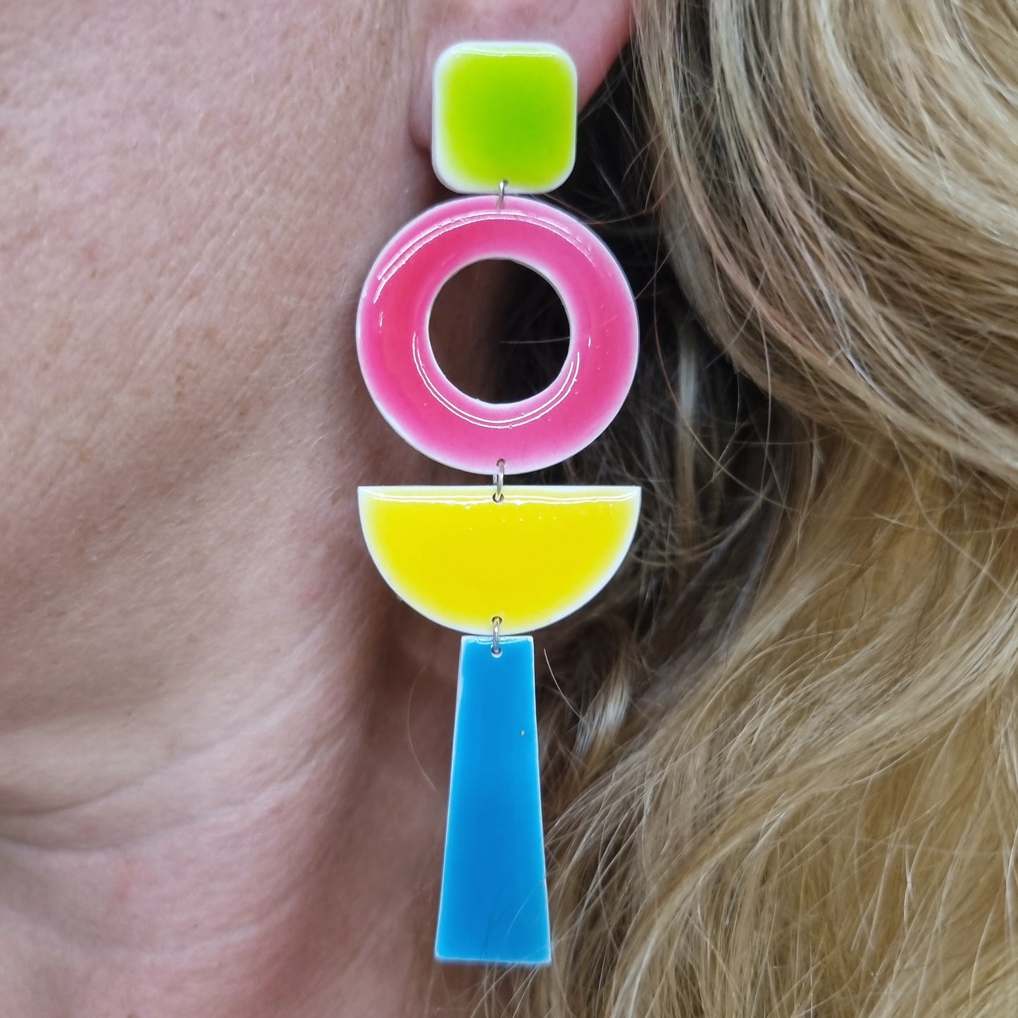 Colorful earrings with pink, yellow, and blue geometric shapes worn by a person.